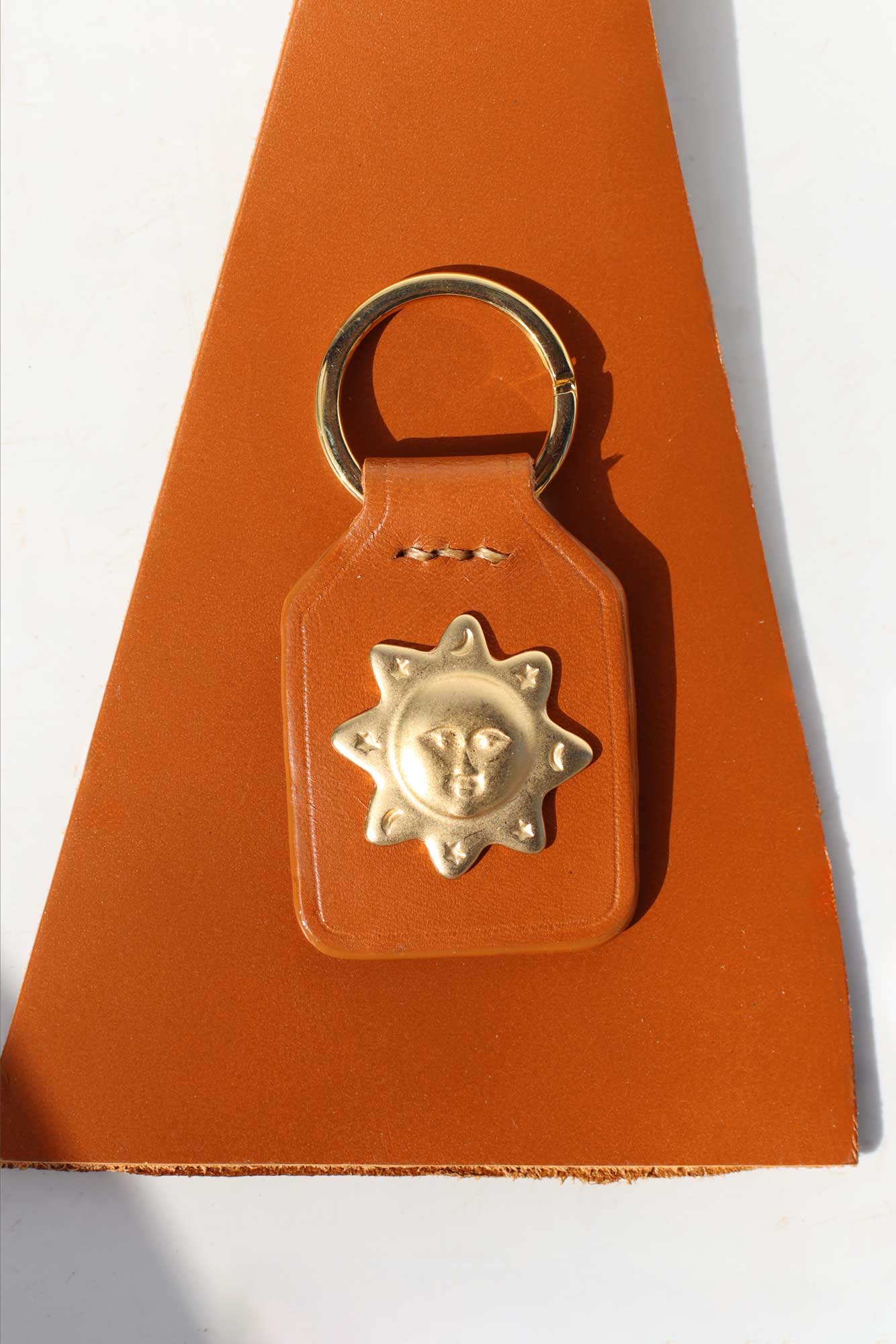 Brown leather keychain with gold sun design on a white background