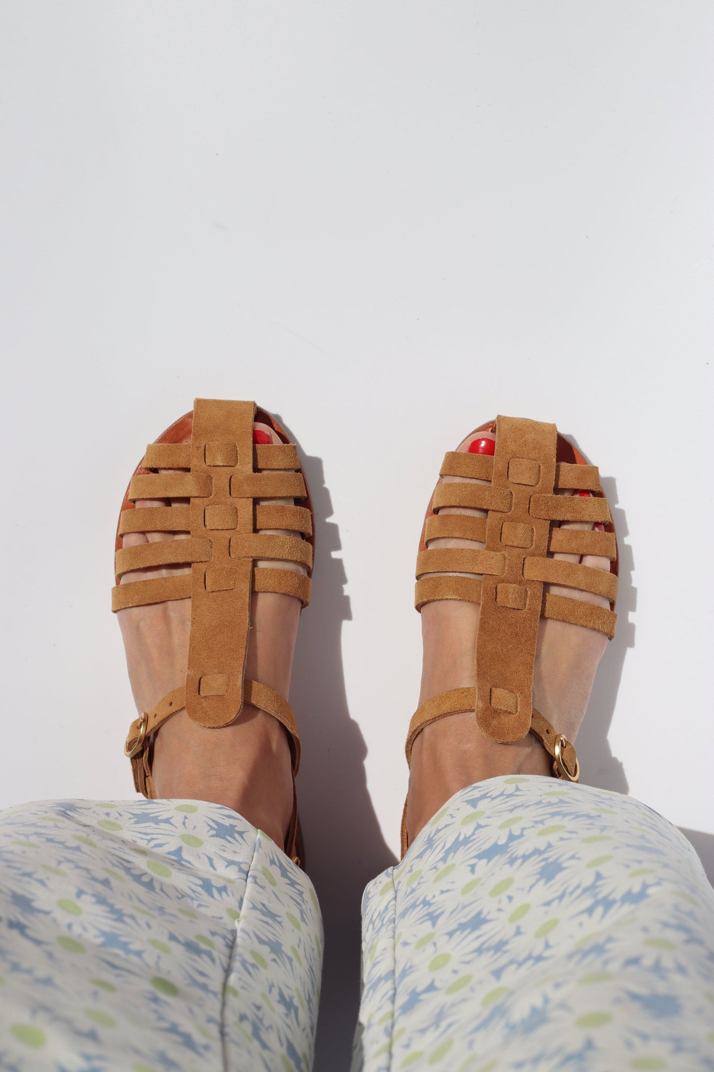 a woman with a flower pant is wearing brown suede sandals