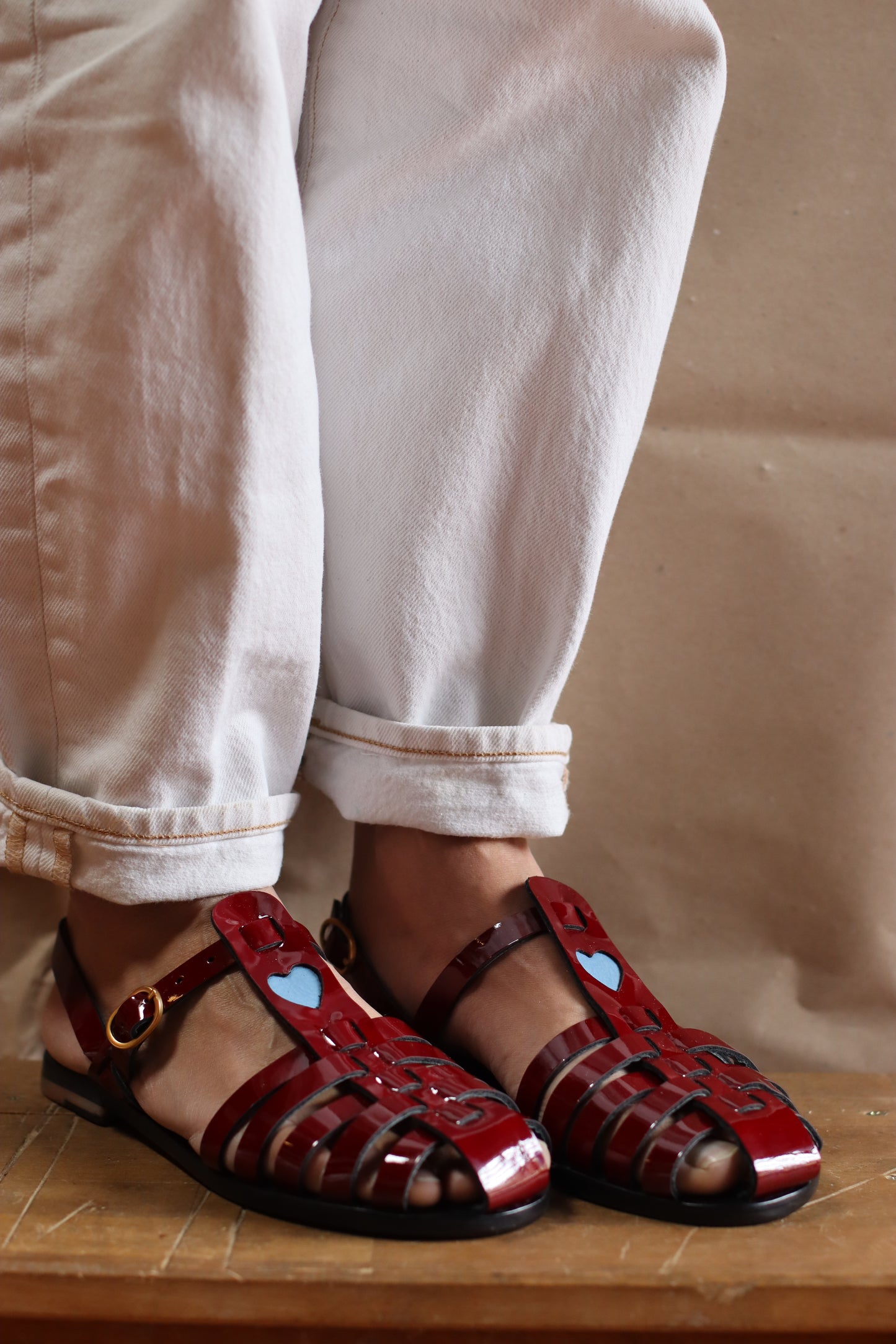 Burgundy patent and blue heart for this leather model of flat sandals, being wear with a pair of white jeans