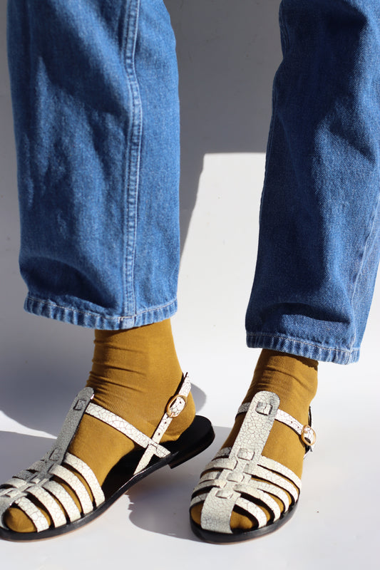Close-up of feet wearing sandals with a person wearing blue jeans and mustard yellow socks.