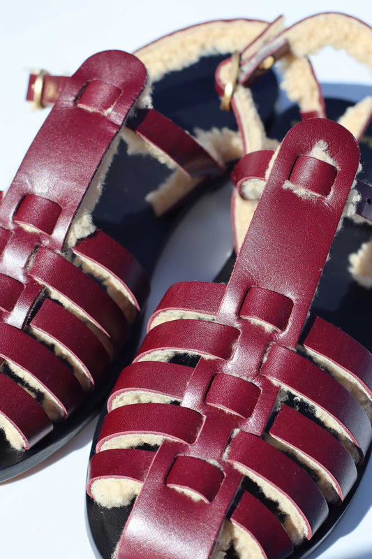 Burgundy leather sandals with woven straps on a white background