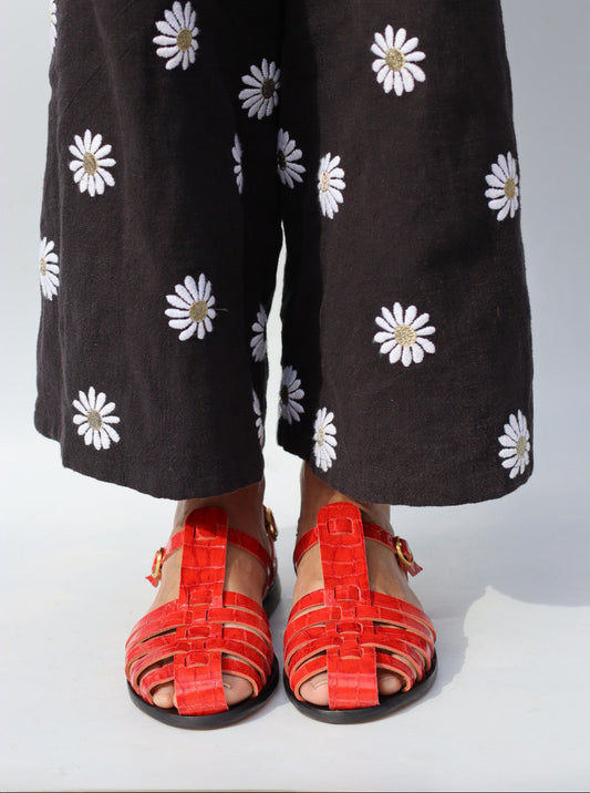 Person wearing black pants with white floral patterns and red sandals on a white background