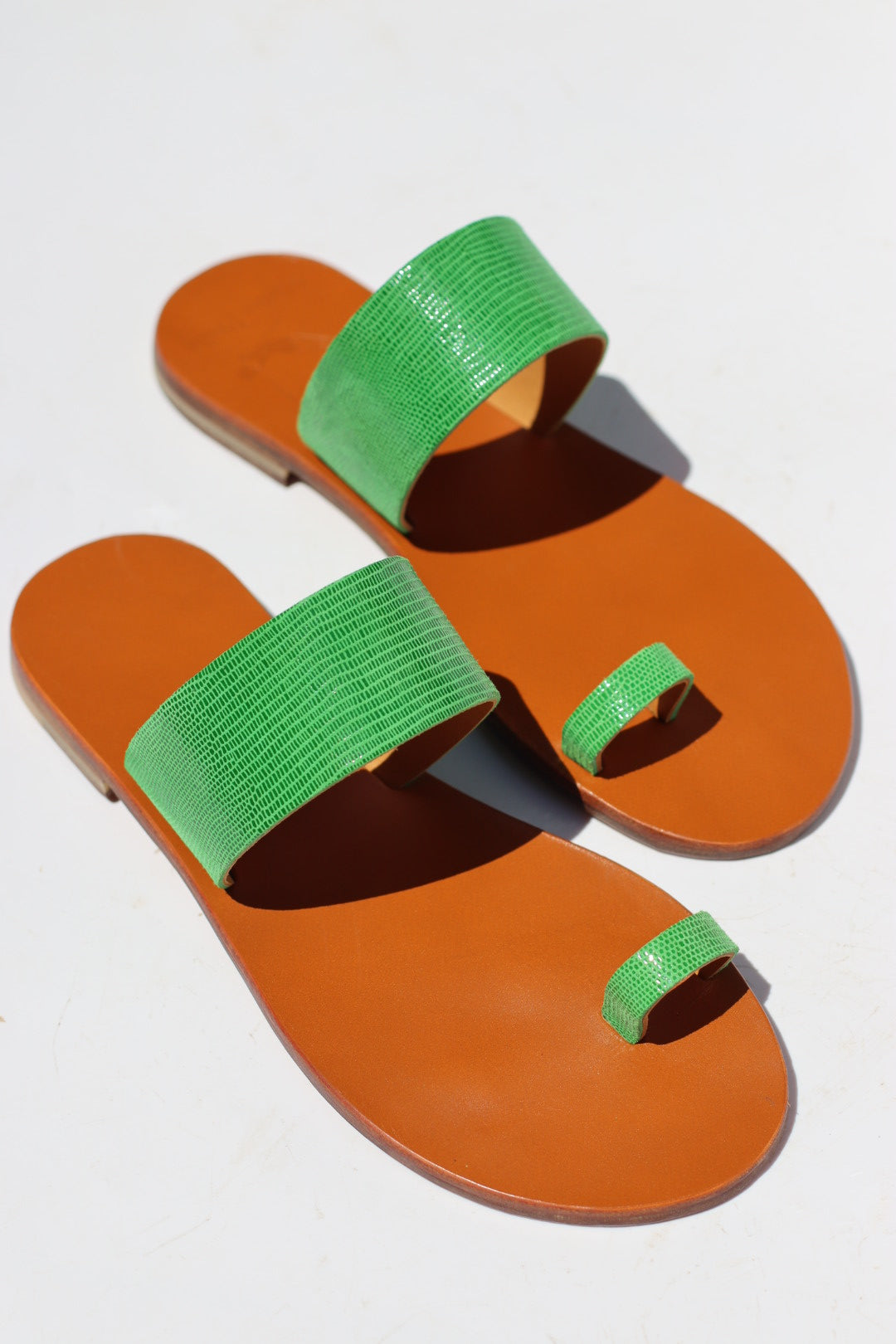 A pair of thong sandals with bright green textured straps and orange-brown footbeds, shown on a plain white background.