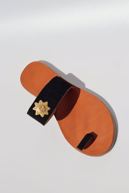Camel sole sandal with a black strap and gold sun on a white background