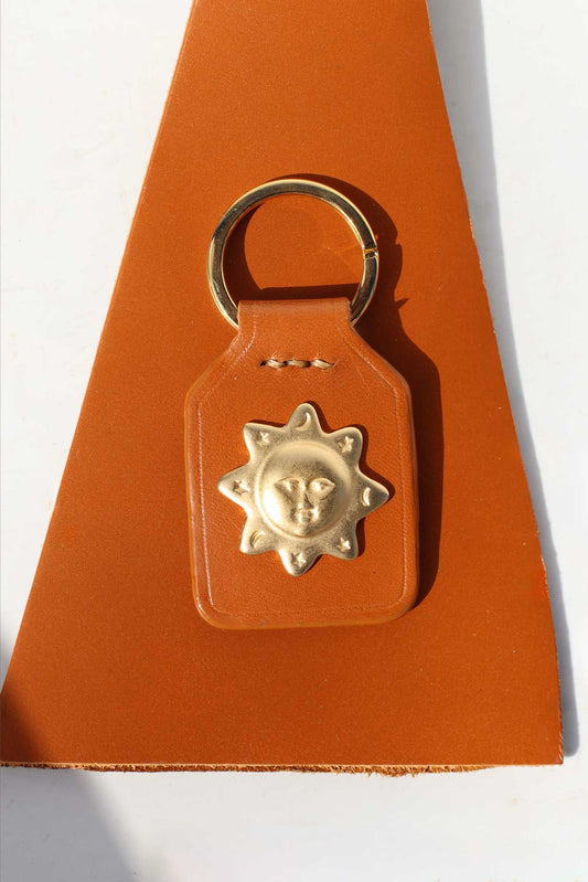 Brown leather keychain with gold sun design on a white background