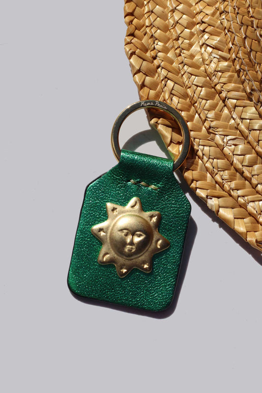 Green leather keychain with gold sun design on a straw hat background