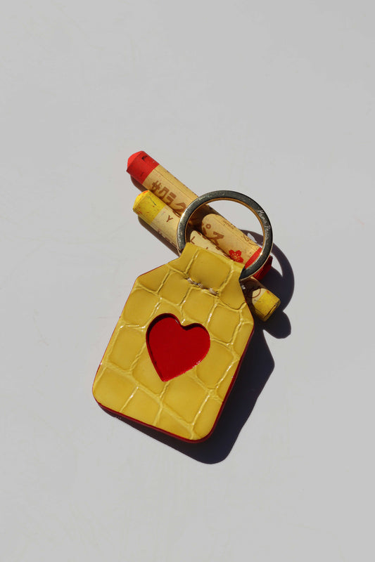 Yellow keychain with a red heart and three crayon-like objects on a light gray background