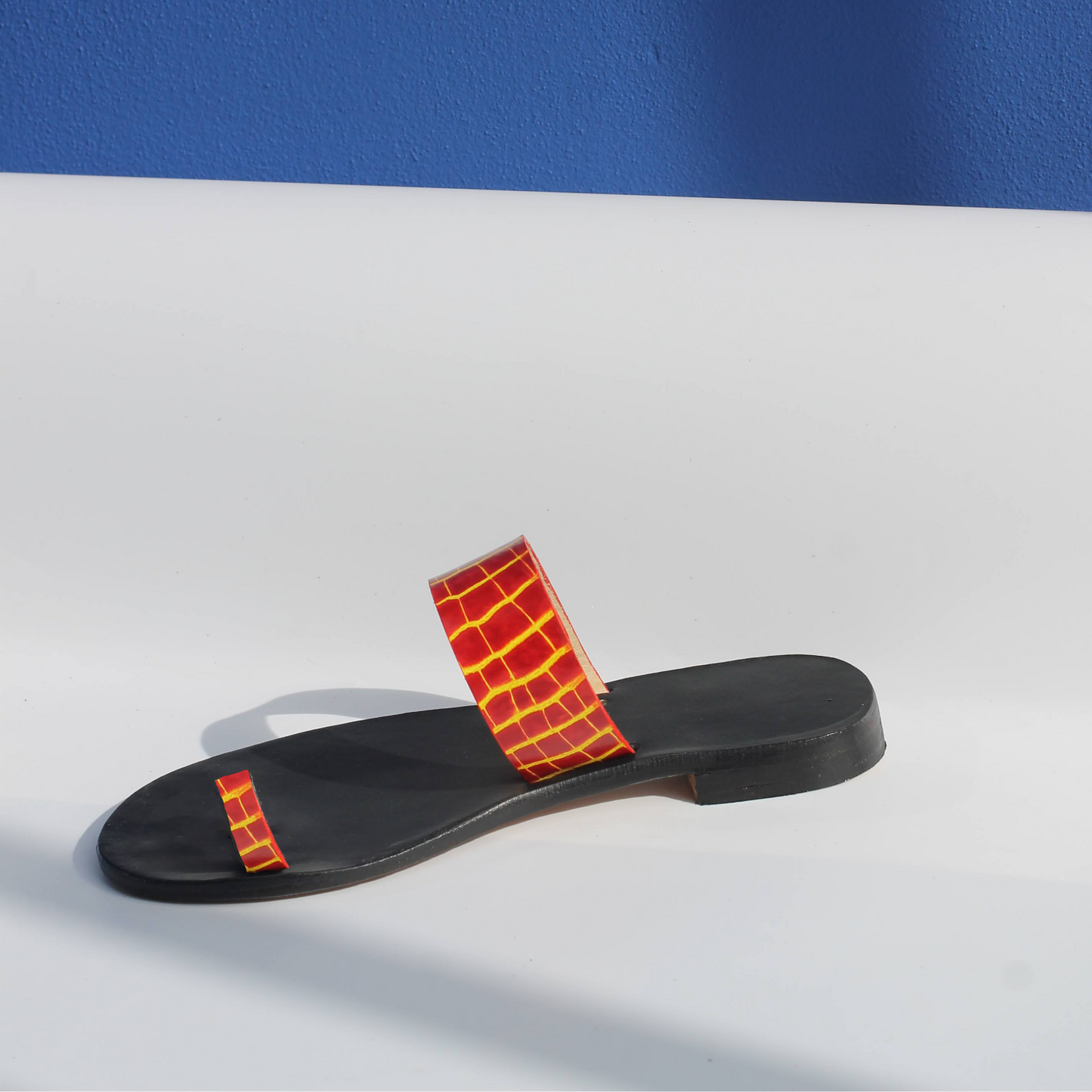 Black sandal with yellow fire strap on a white surface and blue background
