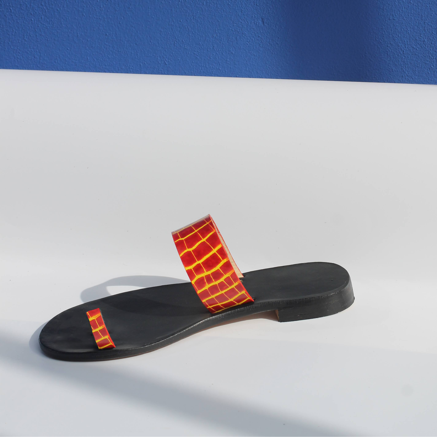 Black sandal with yellow fire strap on a white surface and blue background
