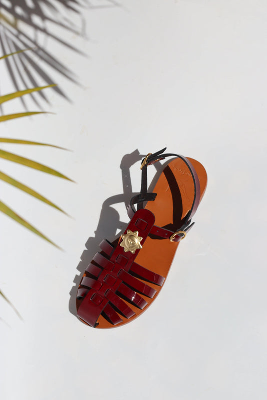 Burgundy sandal with decorative straps on a white background