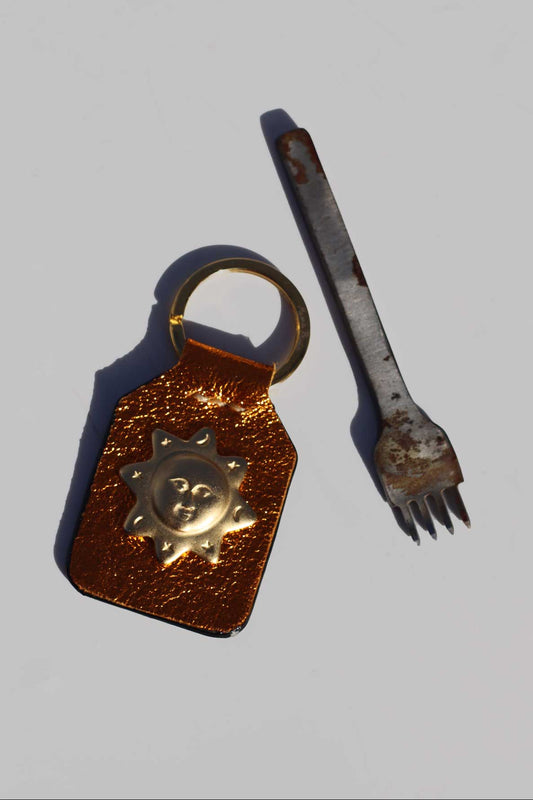 Orange leather keychain with metal clasp and rusty metal fork on a gray background