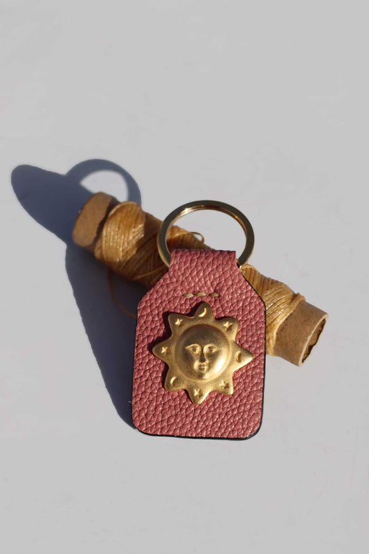 Pink leather keychain with gold sun design on a light gray background